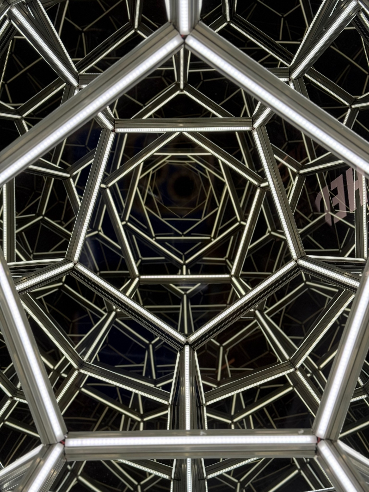 A mirrored illuminated geometric sphere with repeating interconnected forms.