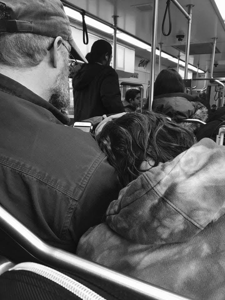A child resting against her father on a crowded train.